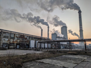 Zdjęcie przedstawia przemysłową elektrownię z wieloma kominami, z których unosi się dym, symbolizując emisje CO2 i obliczanie śladu węglowego firmy zgodnie z GHG Protocol Scope 1 i 2.