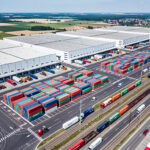 Widok z lotu ptaka na duże centrum logistyczne z kontenerami i ciężarówkami, symbolizujące ESG Orlen i Allegro.