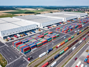 Widok z lotu ptaka na duże centrum logistyczne z kontenerami i ciężarówkami, symbolizujące ESG Orlen i Allegro.